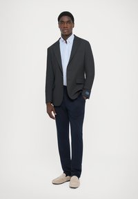 Σκούρο γκρι σακάκι πάνω από ένα ανοιχτό μπλε πουκάμισο με ρίγες, συνδυασμένο με ναυτικές παντελόνες και μπεζ loafers. Το σακάκι διαθέτει ένα κουμπί και δύο τσέπες.