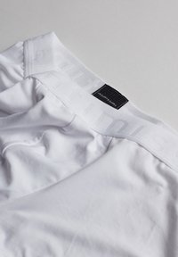 Hvide boksershorts med en blød tekstur. Taljen har subtil branding med et sort mærke, der er fastgjort indvendigt.
