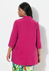Fuchsia tuniek met driekwart mouwen, met zijsplitten. Gladde textuur en eenvoudig ontwerp, gecombineerd met kleurrijke geprinte broek.