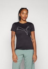 Tricou negru cu mânecă scurtă, fabricat dintr-un material moale, având un logo alb Puma pe față. Croiala este casual și se potrivește perfect cu o pereche de pantaloni verzi deschis.