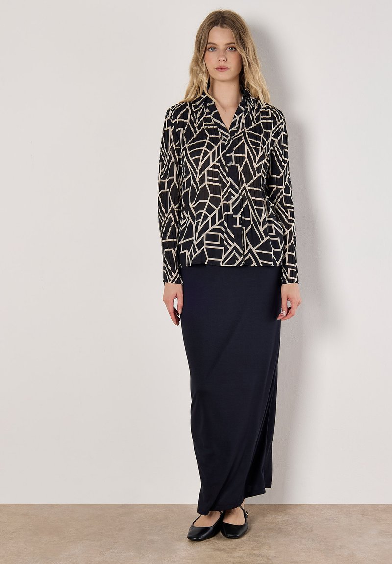 Black and cream patterned blouse with geometric design, paired with a solid black maxi skirt. Smooth fabric, button-down front, long sleeves.