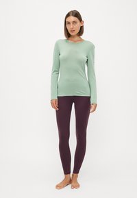 Langermet, mintgrønn topp kombinert med tettsittende, dyp lilla leggings, begge laget av glatt, elastisk stoff.