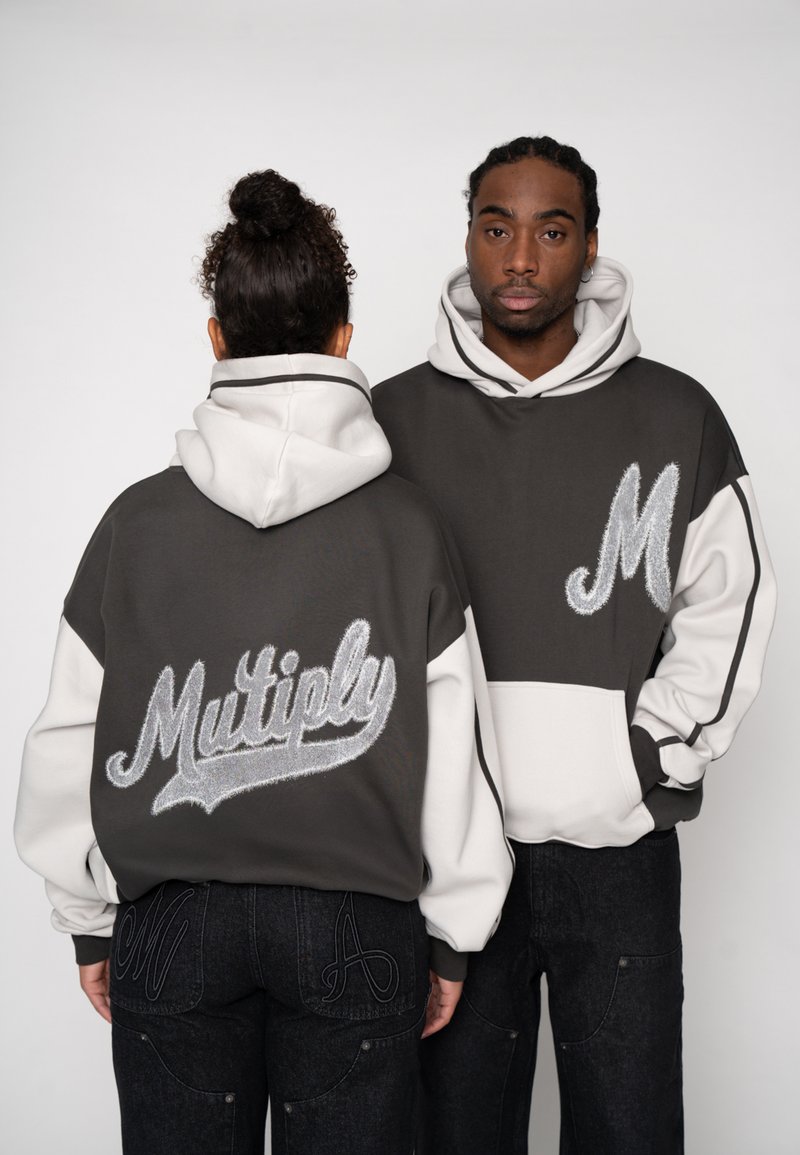 Hanorace supradimensionate în gri închis și alb, cu broderie "Multiply" pe spate și un "M" stilizat pe față. Material din amestec de bumbac.