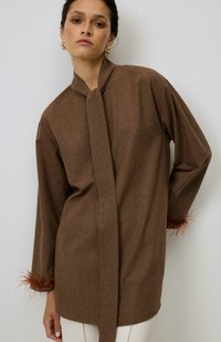 Maglia marrone a maniche lunghe con chiusura a cravatta, caratterizzata da dettagli in piuma testurizzati ai polsini. Tessuto morbido con silhouette rilassata.