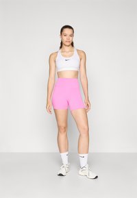 Hvit idretts-BH med svart logo, kombinert med høyt liv rosa shorts. Hvite sokker og lyse joggesko fullfører det sporty antrekket.