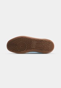 Semelle de chaussure avec motifs circulaires, anneaux concentriques sous la boule du pied, et logo "Puma" dans la zone de la voûte plantaire, matériau en caoutchouc marron.