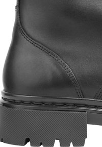 Bota de cuero negro con una textura suave, que presenta una suela de goma resistente y costuras reforzadas a lo largo de las costuras, destacando su durabilidad.