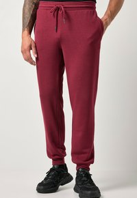 Burgundy sweatpants i mjukt material med dragsko i midjan, slim fit, sidofickor och ribbade ärmslut, i kombination med svarta sportskor.