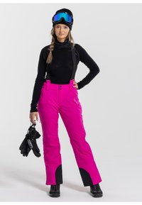 Roze sneeuwbroek met verstelbare bandjes, twee voorkruiken en zwarte accenten aan de zoom, gecombineerd met een zwarte top en handschoenen.