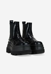 Bottines noires avec une finition en cuir lisse et brillant, des panneaux latéraux élastiques et des semelles en caoutchouc épaisses avec un motif de profondeur.