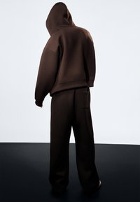 Bruine hoodie met een losse pasvorm, gecombineerd met bijpassende losse broek met een achterzak. Glad, matte textuur.