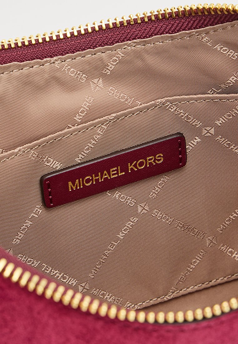 Intérieur en daim d'un sac bordeaux avec fermeture éclair sur le dessus. Doublé de tissu beige avec un imprimé de logo subtil ; accents en matériel doré visibles.