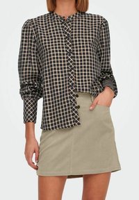 Camicia a quadratini blu navy e crema, con maniche lunghe e colletto alto, abbinata a una mini gonna in corduroy verde chiaro.