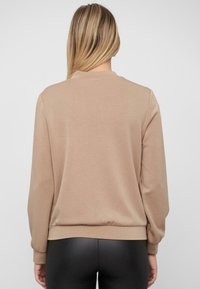 Licht beige lange mouw sweatshirt met een ronde hals, ribbelmanchetten en zoom. Zachte textuur, eenvoudig ontwerp en geen zichtbare merknaam.