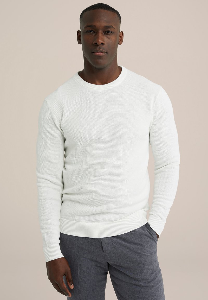 Witte trui met een gestructureerd breipatroon, voorzien van een ronde halslijn en geribde mouwen en onderrand, gedragen met grijze broek.