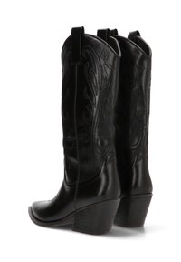 Un par de botas de vaquero de cuero negro con costuras decorativas, tiradores, punteras puntiagudas y tacones apilados, vistas desde un ángulo trasero.