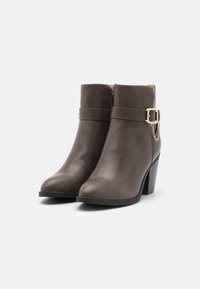Brune faux læder ankelstøvler med firkantet tå, en chunky hæl og en dekorativ kæde på ankelremmen. Glat tekstur, minimalistisk design.