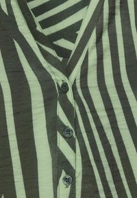 Camicia a maniche corte con strisce zebrate verdi e grigio scuro, design a scollo a v e chiusure con bottoni neri lungo il davanti. Tessuto morbido.