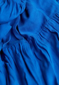 Tissu bleu avec une texture lisse, présentant des sections froncées et plissées. Le matériau semble léger et légèrement extensible.