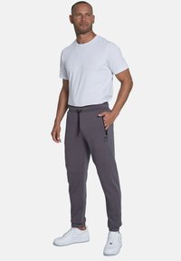 Gray jogger pants with a drawstring waist, side zip pocket, and tapered fit, paired with a plain white short-sleeve shirt and white sneakers.