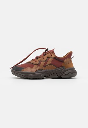 Chaussure de sport basse en tons marron et rouille, semelle texturée, devant lacé, avec panneaux superposés en tissu et cuir.