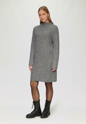 Graues Strickkleid mit hohem Kragen, langen Ärmeln und gerader Passform, kombiniert mit schwarzen Schnürstiefeln im Kampfstil. Glatte Textur über das gesamte Kleidungsstück.