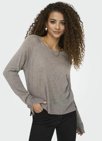 Maglione a maglia grigio chiaro con un design morbido, spalle scese, fessure laterali e tessuto strutturato. Abbinato a pantaloni neri.