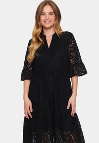 Black lace dress with a v-neck and tiered design. Features flared sleeves and intricate floral patterns throughout. Breathable fabric texture.
