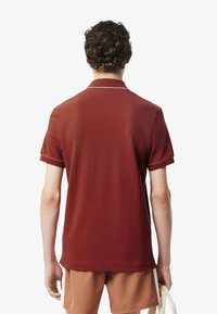 Herrpolo i djupröd med kort ärm, utrustad med vit kantning längs kragen och ärmarna, samt en avslappnad passform.