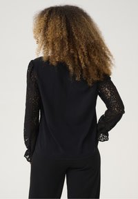 Czarna bluzka z długimi rękawami z wzorzystej koronki, z gładkim tyłem. Teksturowane detale z koronki dodają wizualnego kontrastu do tkaniny.