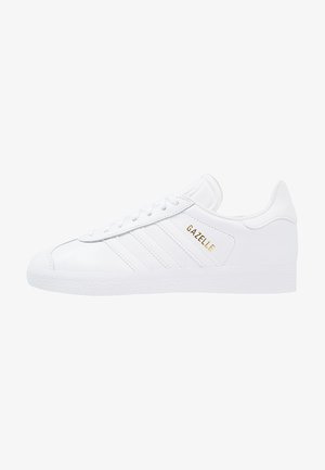 White leather sneaker with three side stripes, textured rubber sole, and gold "GAZELLE" branding on the side. Features lace-up design.