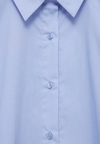 Camicia col colletto azzurro chiaro vista frontale con patta centrale dei bottoni che mostra tre bottoni blu trasparenti e cuciture visibili.