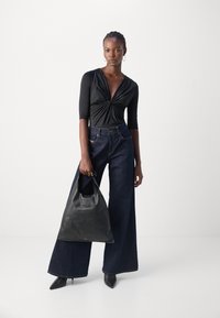 Svart langermet topp med vridd design, høyt liv mørk denim vide bukser og en glatt svart skinnveske.