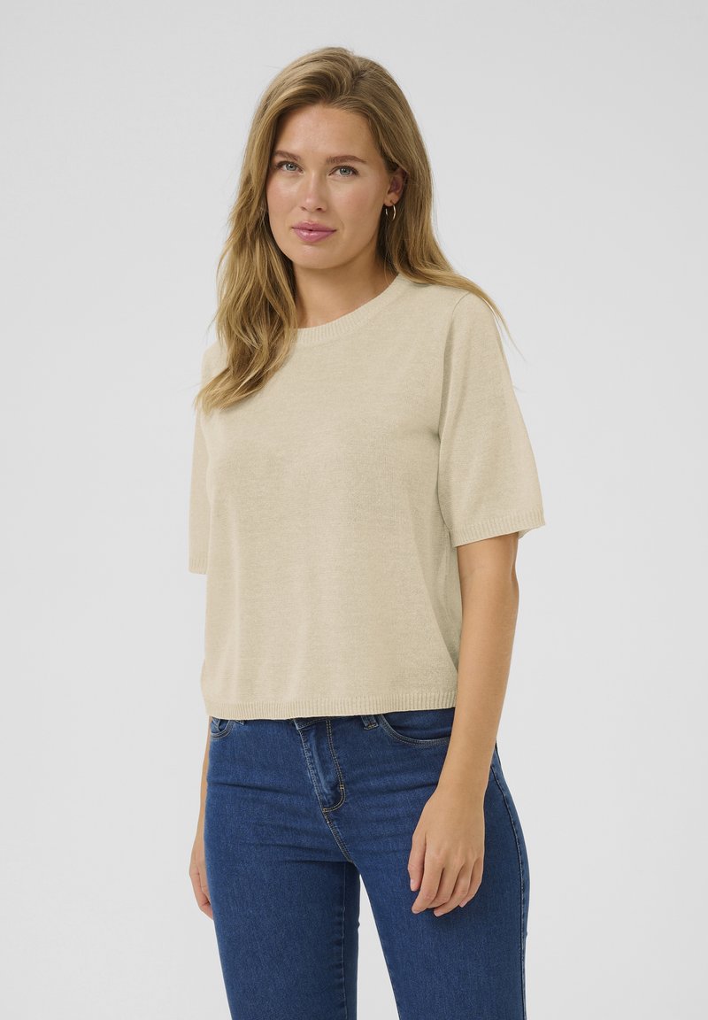 Pull en tricot beige à manches courtes, avec un col côtelé et une coupe décontractée. Associé à un jean en denim bleu pour un look décontracté.