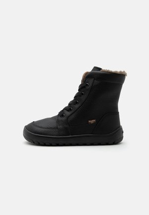 Botte d'hiver noire en cuir avec lacets, doublure en fourrure, semelle texturée et petite étiquette marron "froddo tex" sur le côté.