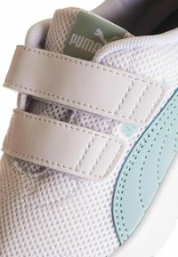 Zapatillas de malla blancas con dos correas de Velcro blancas, acentos en azul claro, panel lateral texturizado y una etiqueta de marca verde en la lengüeta.