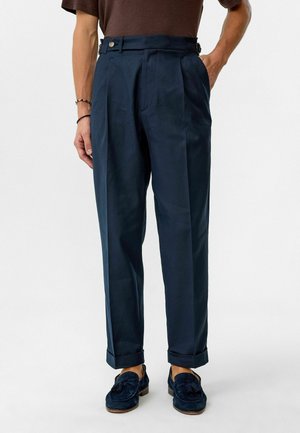 Marineblauwe high-waisted broek met plooien, voorzien van zijzakken en verstelbare taillebanden. Glad stoffen met een getailleerde pasvorm.