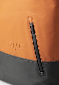 Oranje en grijze stoffen tas met een gestructureerd oppervlak, voorzien van een zwarte rits en een reliëflogo op het oranje gedeelte.