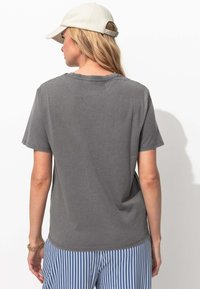 T-shirt en coton gris à manches courtes et coupe décontractée, associée à un pantalon rayé bleu et blanc. Elle présente un col rond et une texture douce.