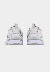 Ζευγάρι λευκών και ασημένιων αθλητικών παπουτσιών Puma, εμφανιζόμενο από πίσω σε απλό, ανοιχτό φόντο.