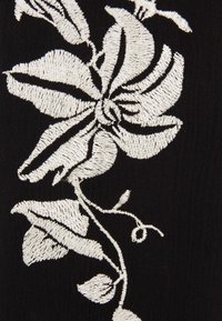 Schwarzer Stoff mit aufwendiger weißer Blumenstickerei, die detaillierte Blütenblätter und Blätter mit einem strukturierten, erhabenen Stichmuster zeigt.