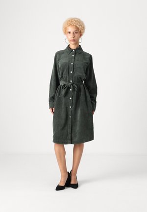 Robe chemise en corduroy vert foncé avec des manches longues, un devant boutonné et une taille à nouer. Elle présente une texture côtelée verticale et des poches latérales.
