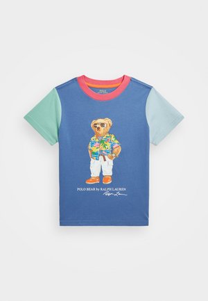T-shirt bleu à manches courtes avec des manches vertes et bleu clair, col rouge, et un ours portant des lunettes de soleil et des vêtements tropicaux sur le devant.