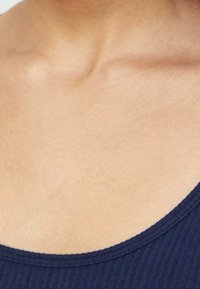 Zbliżenie górnej części klatki piersiowej i obszaru obojczyka osoby w ciemnoniebieskiej, prążkowanej bluzce.
