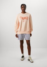 Sudadera melocotón con "FRANCIA" y el logo de Nike, combinada con shorts de rayas blancas y negras, con un ajuste relajado y textura suave.