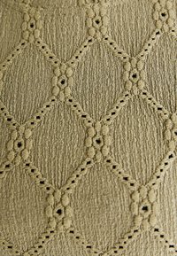 Textured fabric featuring a beige, diamond-shaped pattern with raised accents and small openings, creating a layered, detailed appearance.