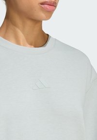 Jasnoszara bluza z luźnym krojem, z teksturowanym logo w trzy paski na klatce piersiowej i klasycznym dekoltem typu crew neck.