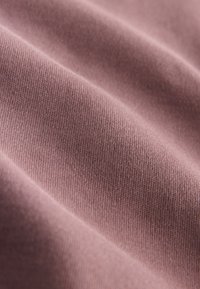 Textilná tkanina v tlmenej fialovej farbe s hladkou textúrou, ktorá ukazuje jemné diagonálne línie a mäkký, tkaný vzhľad.