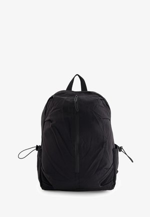 Schwarzer Nylon-Rucksack mit zentralem Reißverschluss, verstellbaren Seitentaschen und Tragegriff oben, aufrecht stehend vor weißem Hintergrund.