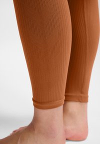 Braune, gerippte Leggings mit einem Chevron-Muster und einer enganliegenden Passform, die knapp über dem Knöchel enden. Weicher, dehnbarer Stoff sichtbar.